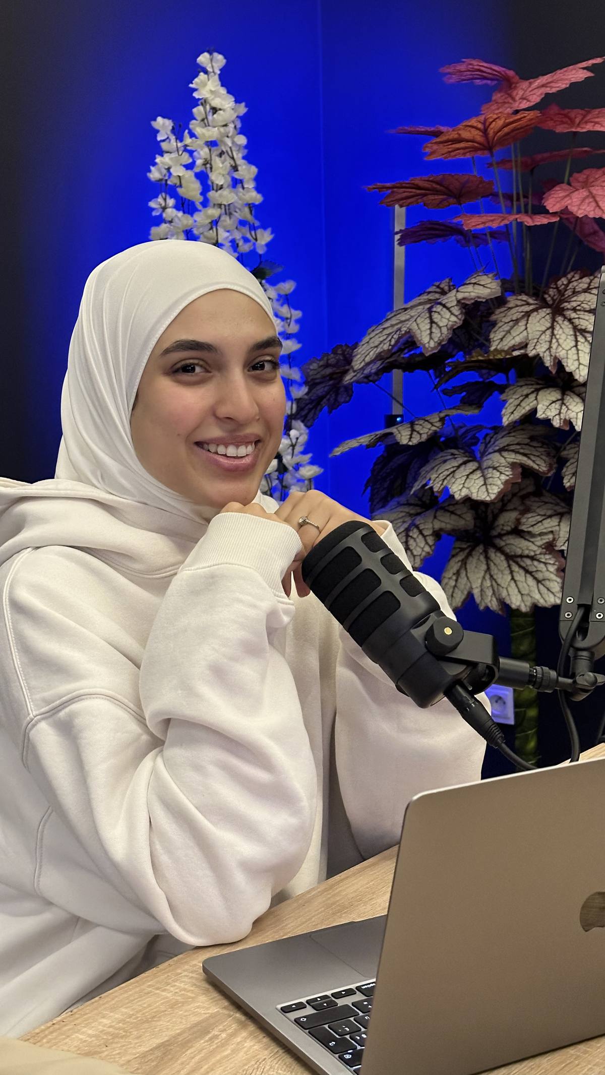 Amal, voilée, sourit devant un micro et un ordinateur, pour illustrer la présentation d’une idée de podcast.